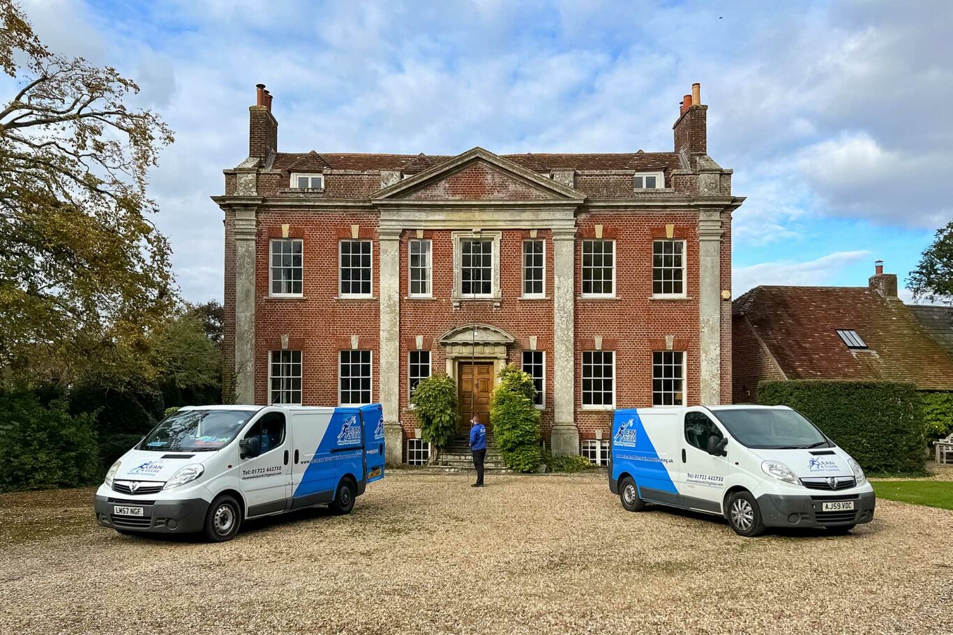 Man window cleaning a large stately home with two vans outside.