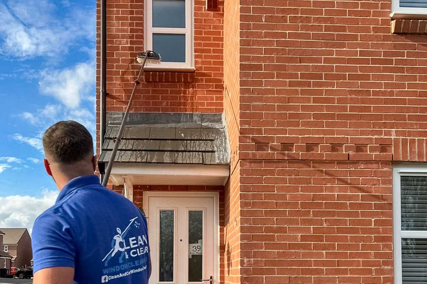 Man wearing a blue polo shirt cleaning first floor window.