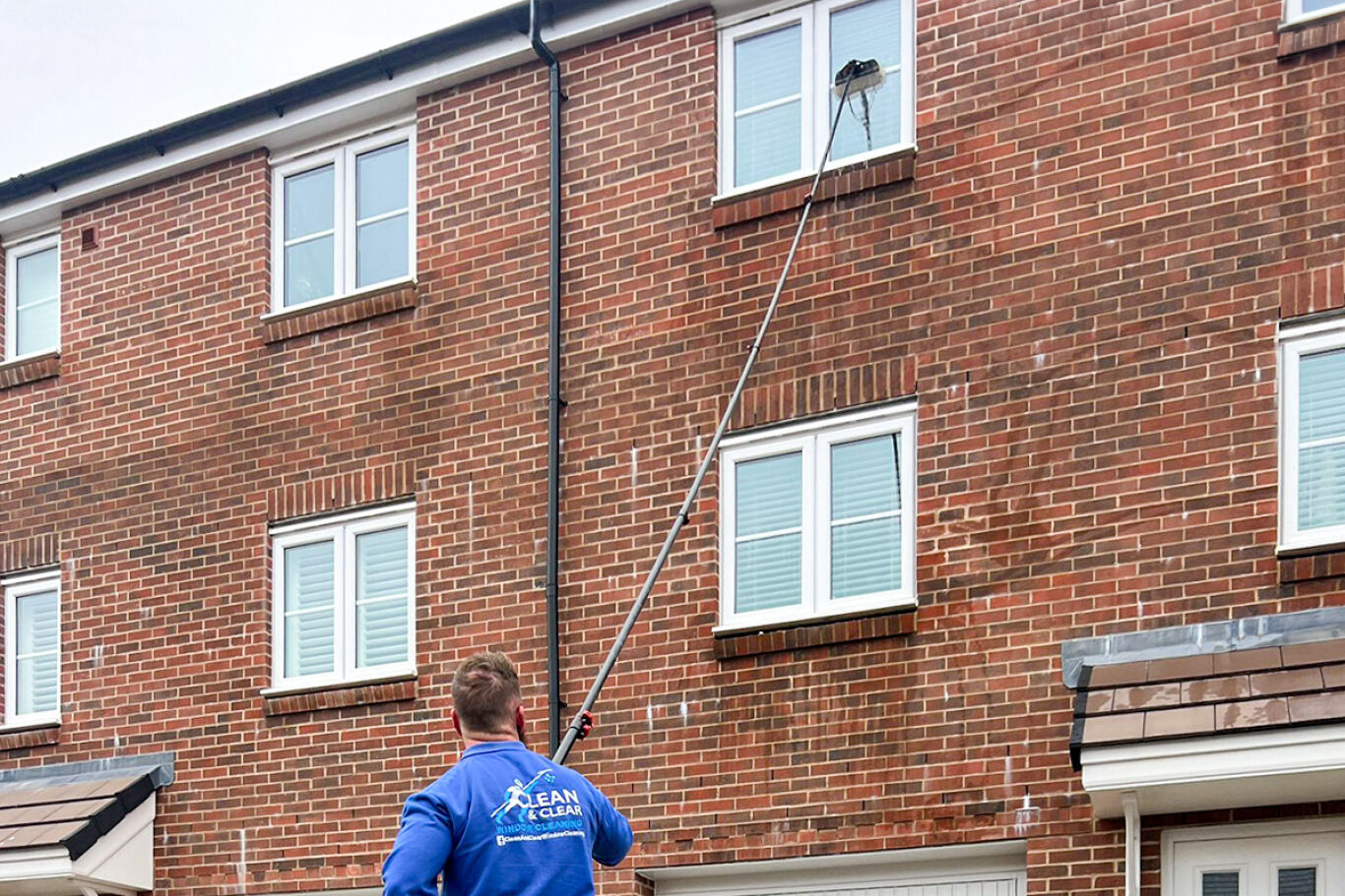 Man wearing a blue jumper cleaning the window of an stately home.