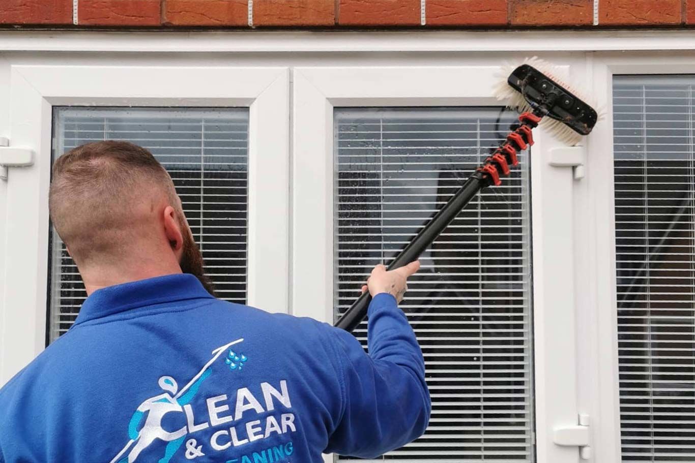 Man wearing a blue jumper with the clean and clear window cleaning logo on the back cleaning a window.