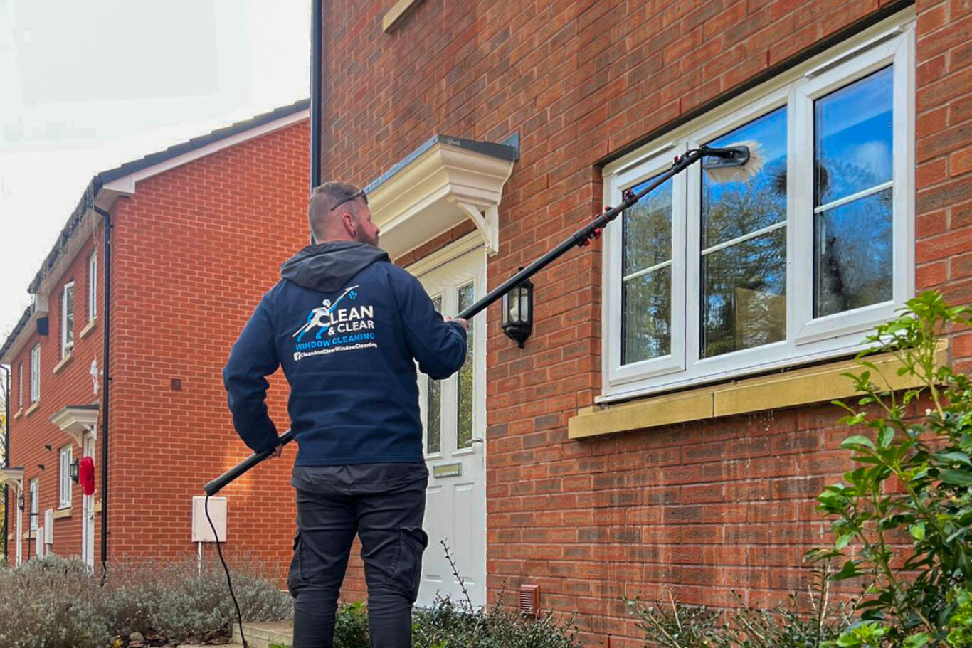 Man in blue polo shirt cleaning ground floor window.