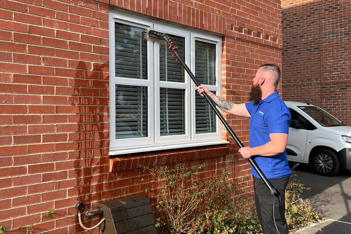 Man wearing a blue jumper with the clean and clear window cleaning logo on the back cleaning a window.