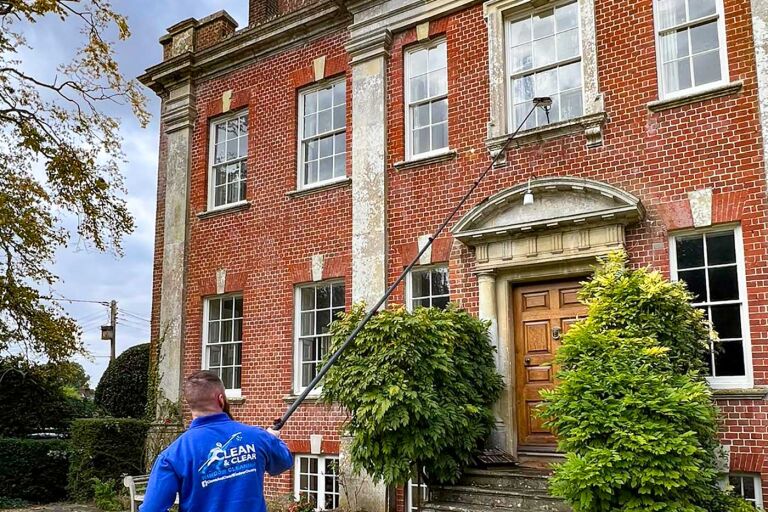 Man wearing a blue jumper cleaning the window of an stately home.